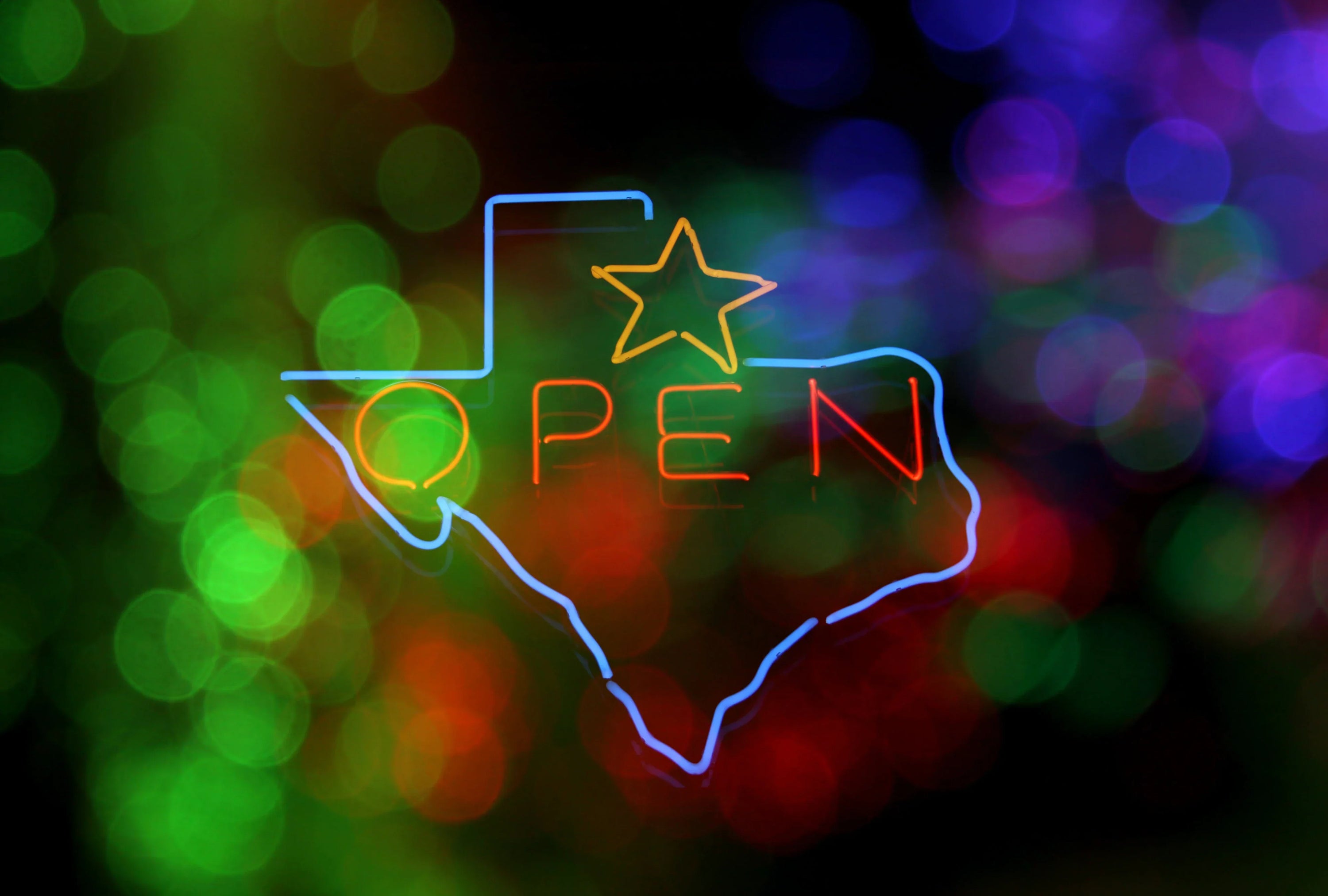 Neon sign in the shape of Texas and the word “open” with green bokeh.