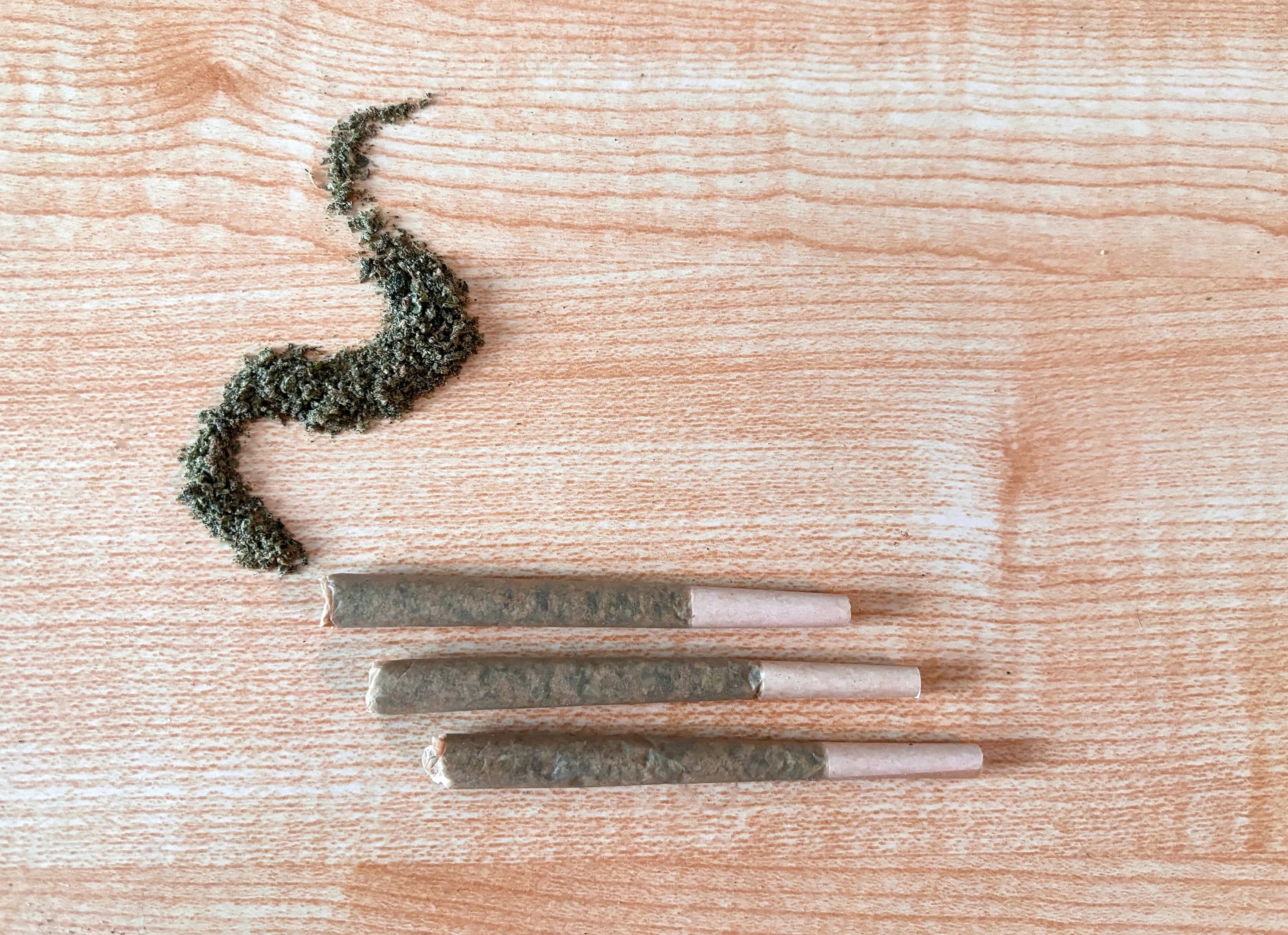 Pre-rolls on a wooden table and loose bud in the shape of smoke