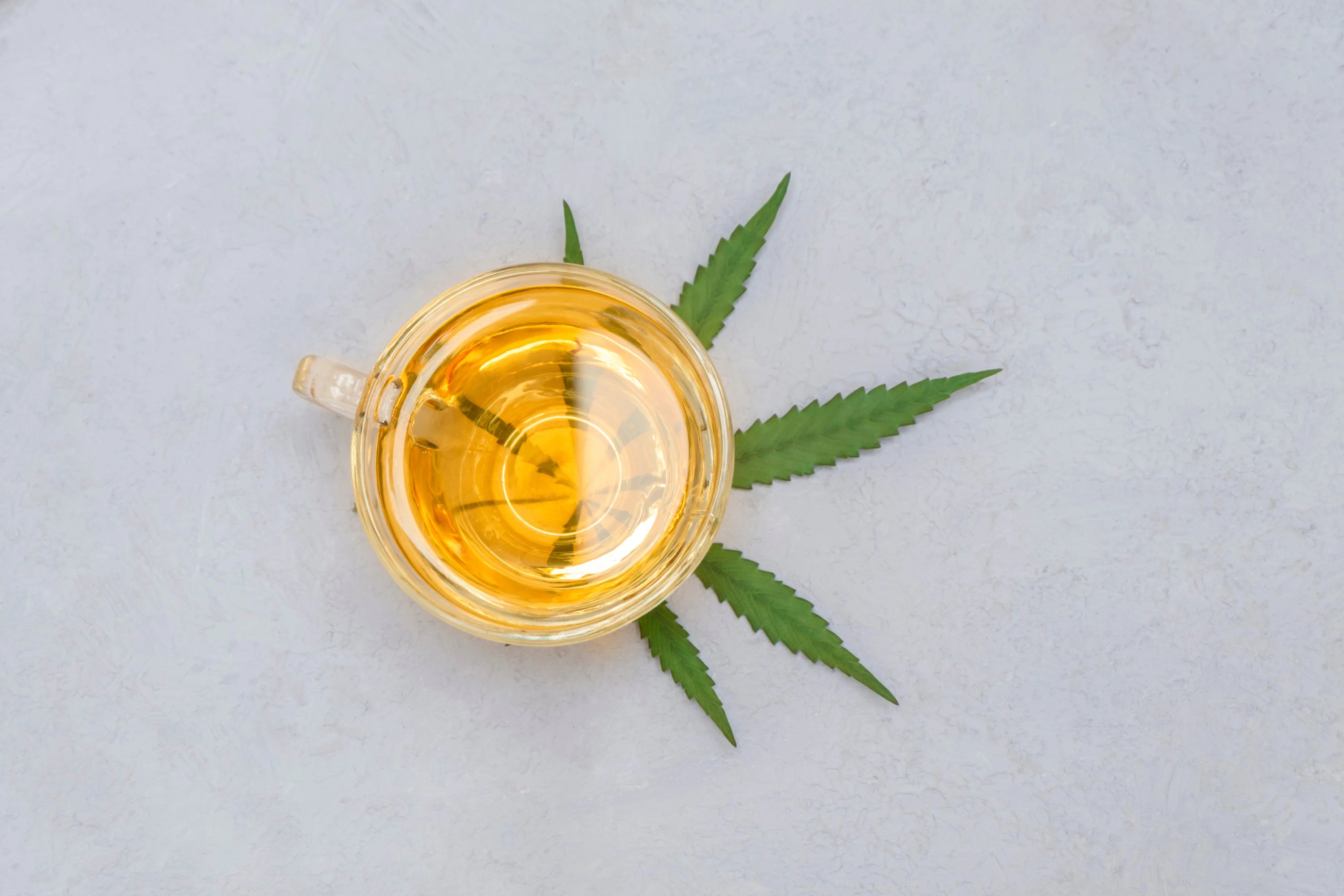 Top view of cup of cannabis tea with green marijuana leaf on stone tabletop